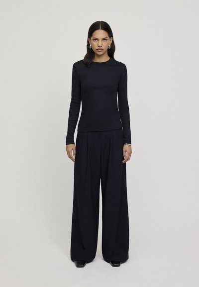 Top lung cu mânecă lungă de culoare bleumarin, cu guler rotund, asortat cu pantaloni largi bleumarin. Ambele piese au o textură netedă și un design minimalist.