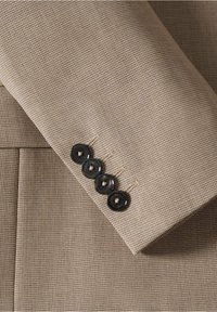 Giacca di un vestito color beige chiaro con maniche che presentano quattro bottoni neri con una leggera lucentezza, dettagliata con un delicato motivo a scacchi houndstooth.
