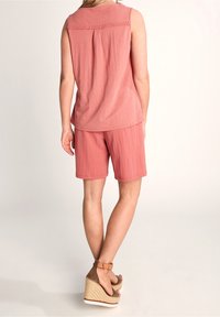 Haut sans manches rose avec un détail tressé au dos, associé à un short assorti. Porté avec des sandales compensées marron, mettant en valeur des textures douces.