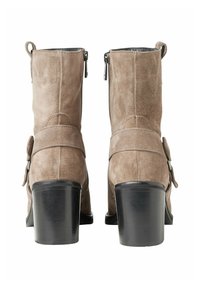 Brown suede ankle boots with a round toe, vertical zippers, and side strap accents. Chunky black heel adds stability and height.