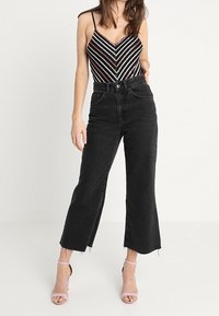 Jean noir taille haute avec une jambe évasée et raccourcie. Le tissu a une texture en denim, avec des ourlets bruts aux chevilles et des poches classiques.