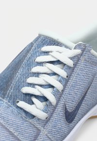 Tenisky s modrým džínovým vzorem a bílými tkaničkami, se světle modrým interiérem a tmavě modrým logem Nike swoosh. Plochý, zaoblený design špičky.