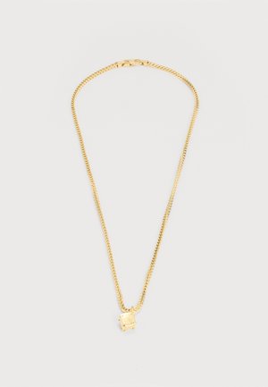 Złoty naszyjnik z łańcuszkiem i kwadratowym wisiorkiem ozdobionym małym, przezroczystym kamieniem szlachetnym, ułożony płasko na jasnoszarym tle.