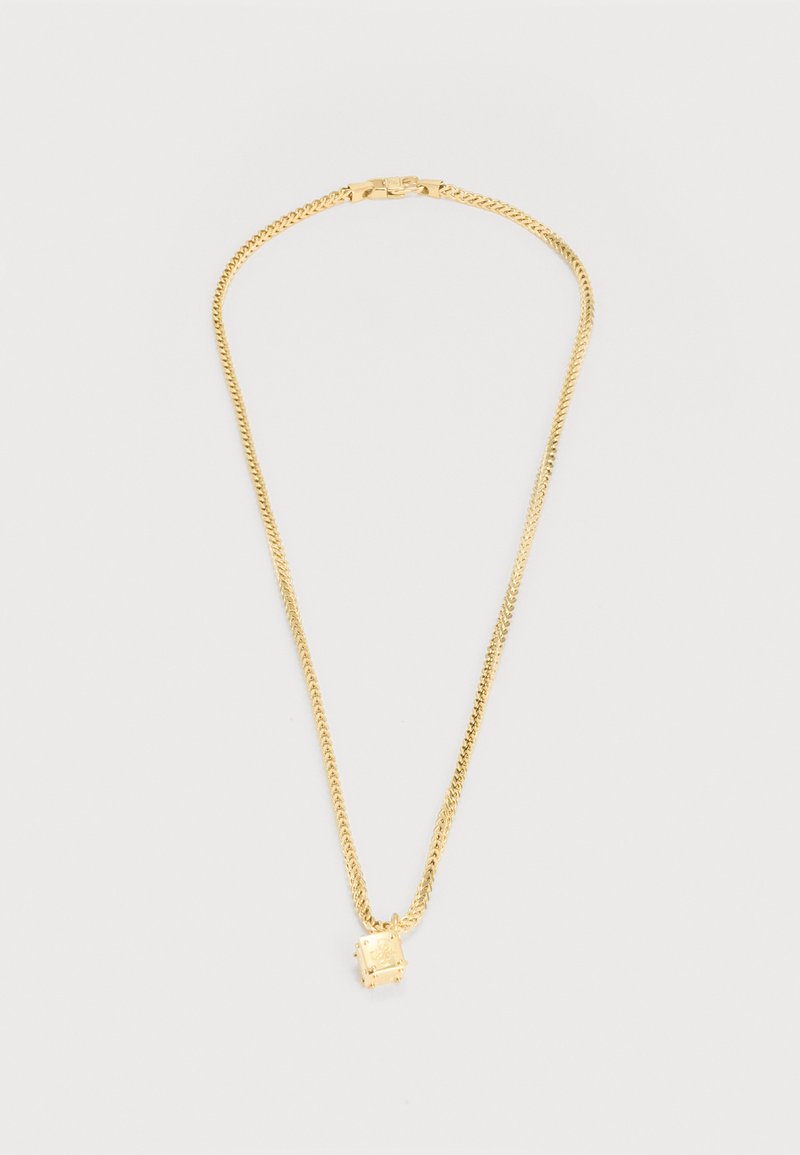 Goldene Halskette mit quadratischem Anhänger, der einen kleinen klaren Edelstein trägt, flach auf einem hellgrauen Hintergrund dargestellt.