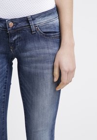 Mörkblå denimjeans har en medelhög midja, slät textur och lätt blekning. Accentuerade med en kopparknapp och subtila sömmar.