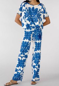 To-delt outfit med en løs, kortærmet top og bredbenede bukser i hvide og blå blomsterprint. Blød, glat tekstur.