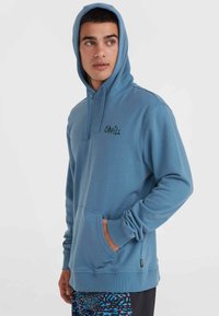 Blauwe hoodie met een voorzak, trekkoord en geborduurd logo. Lange mouwen en ribgebreide manchetten. Zacht materiaal met een gladde textuur.