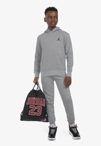 Szürke pulóver elülső zsebbel és fekete logóval, hozzáillő szürke melegítőnadrág, fekete húzózsinóros táska, piros "JORDAN 23" felirattal, fekete sportcipő.