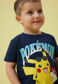 Camiseta de algodón azul marino con gráfico de Pikachu usando gafas de sol, texto "POKÉMON" en azul y blanco, mangas cortas y cuello redondo.