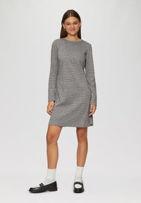 Graues langärmliges Kleid mit einem dezenten Karomuster, knielang, aus weichem Stoff. Getragen mit schwarzen Slippern und weißen Socken.