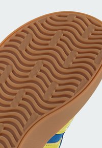 Semelle de chaussure en caoutchouc à texture ondulée, principalement brune avec des accents orange. Présente un motif de grip pour la traction et la durabilité.
