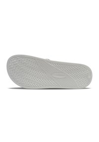 Semelle de chaussure en caoutchouc blanc avec un motif en chevron texturé et des accents de prise circulaires. Présente un logo discret au centre.