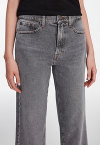 Jeans de mezclilla gris con un diseño de pierna recta, que cuentan con un cierre de botón, bolsillos frontales y un ligero desgaste. Textura suave con costuras visibles.