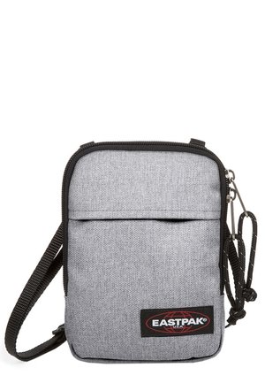 Sac bandoulière en tissu gris avec une surface texturée, fermeture zippée, poche avant, sangle réglable et accent logo rouge et noir.