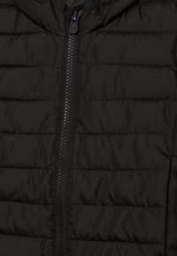 Tissu matelassé noir avec une fermeture éclair centrale sur une veste ou un manteau rembourré, présentant des lignes de couture horizontales.