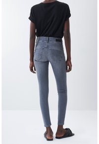 Jeans ajustados gris oscuro con cintura alta, con bolsillos traseros y una textura suave y elástica de mezclilla. Combinados con una camiseta negra de mangas remangadas.