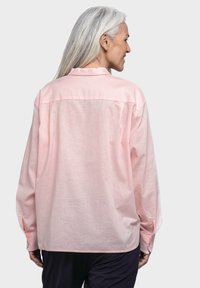 Light pink long-sleeved shirt with a back yoke. Features a collared neckline and buttoned cuffs, made from a textured fabric.