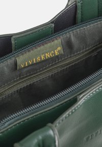 Innenansicht einer dunkelgrünen Ledertasche mit einer schwarzen Stoff-Reißverschlusstasche und einem grünen Etikett mit der Aufschrift „VIVISENCE“ in Gelb.
