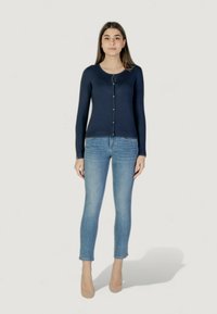 Cardigan bleu marine à boutons avec des manches longues, texture côtelée, encolure ronde, associé à un jean skinny bleu clair et des talons beiges.