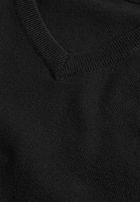 Čierny pletený sveter s výstrihom do V, rebrovaným golierom a hladkou textúrou. Tkanina pôsobí mäkko a ľahko.