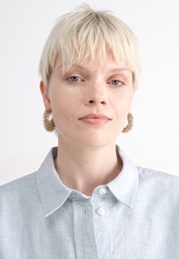 Boucles d'oreilles en argent avec un design en spirale texturé. Chemise boutonnée à rayures bleu clair et blanche avec col. Fond clair.