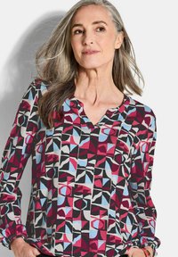 Langärmelige, gemusterte Bluse in Rot, Blau und Schwarz mit geometrischen Formen. Mit V-Ausschnitt und elastischen Bündchen. Leichtes Material.