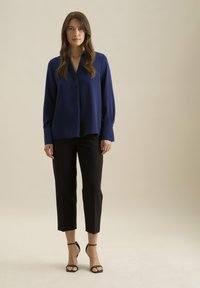 Blusa blu navy con vestibilità morbida, maniche lunghe e mezza abbottonatura, abbinata a pantaloni neri a 3/4 e sandali neri con tacco.