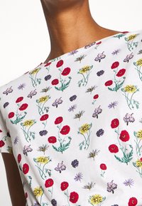 T-shirt en coton avec un fond blanc présentant un motif floral de coquelicots rouges, de marguerites jaunes et de fleurs violettes, à manches courtes et à encolure large.