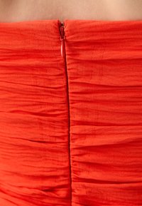 Rød off-shoulder kjole med teksturerte folder og en skjult glidelås bak. Glatt stoff med en tettsittende fasong.
