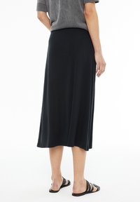 Falda midi negra con textura suave y fluida. La cinturilla se asienta cómodamente en la cintura, combinada con sencillas sandalias negras.