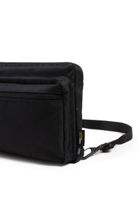 Bolsa de tela negra con dos bolsillos frontales con cremallera, correa ajustable y esquinas reforzadas. Cuenta con una etiqueta de tela con el nombre de la marca y detalles del material.