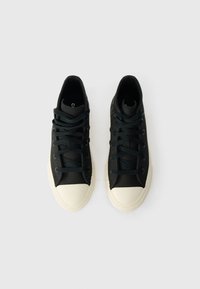 Melna augsto tenisa apavu pāris ar baltām gumijas pirkstu daļām un zoleņiem uz baltas fona.