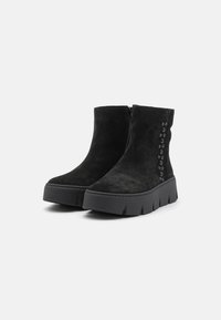 Bottes chelsea en suède noir avec une semelle épaisse, dotées d'une fermeture éclair sur le côté et de clous décoratifs sur un côté.