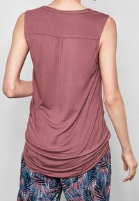 Sleeveless mauve top with back pleat detail worn with patterned pants featuring blue and pink tropical leaves.