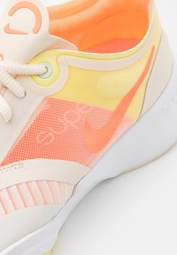 Sportovní obuv Nike s vrškem z prodyšné síťoviny v růžové, žluté a broskvové barvě s bílými akcenty. Obsahuje zaoblenou špičku, tkaničky a detaily loga.