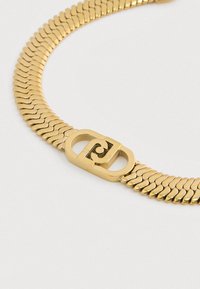 Gullkjede med flate, sammenkoblede lenker og en dekorativ, rektangulær spenne som har et svulmønster.