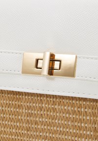 Biała teksturowana skóra z złotym prostokątnym zapięciem i plecioną słomkową podstawą. Posiada widoczne szwy i gładkie akcenty powierzchni.