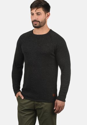 Schwarzes Langarmshirt aus strukturiertem Stoff mit Rundhalsausschnitt und Raglanärmeln; hat einen kleinen Lederpatch am Saum.