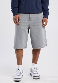 Shorts de mezclilla gris claro con un ajuste holgado, corte recto y dobladillo deshilachado, combinados con zapatillas blancas con acentos grises.