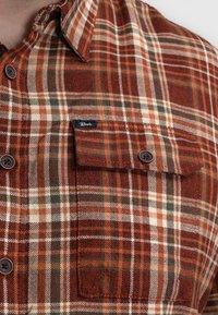 Geruiten shirt in tinten van roest, crème en groen, gemaakt van flanel. Beschikt over twee borstzakken en bruine knopen. Merktag zichtbaar op de zak.