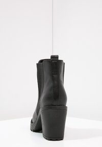 Czarne skórzane botki do kostki z elastycznymi panelami bocznymi i grubym obcasem. Gładka tekstura i zaokrąglony kształt przodu, z pętelką na tyle.