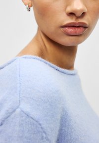 Pull en tricot bleu clair avec un col rond, une texture douce et des détails de couture subtils le long des épaules. Rehaussé par une finition lisse.