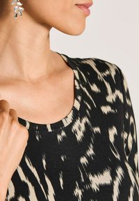 Vrouw in een zwart en beige gestreepte top met ronde halslijn en hangende zilveren edelsteenoorbellen, getoond van nek tot borst.