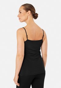 Canotta nera con spalline regolabili, design aderente, texture liscia e dettaglio arricciato sul retro. Abbinata a leggings neri.