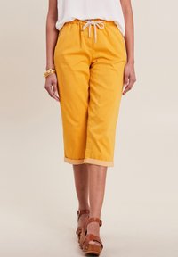 Gele, geknipte broek van katoen, met een koordjes tailleband, omgeslagen mouwen en een gladde textuur. Draag met bruine sandaalhakken.