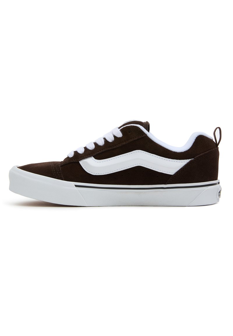 Brune semskede sneakers med hvite snørebånd og sidestrek, med en hvit gummisåle og svart aksentlinje. Enkelt design med pull-tab bak.