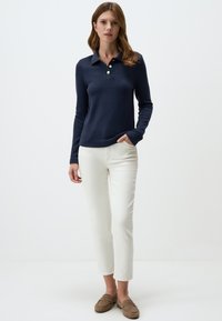 Marineblauw poloshirt met lange mouwen, een kraag en een knoopsluiting met drie knopen, gecombineerd met witte, cropped broek en bruine loafers. Eenvoudig ontwerp.