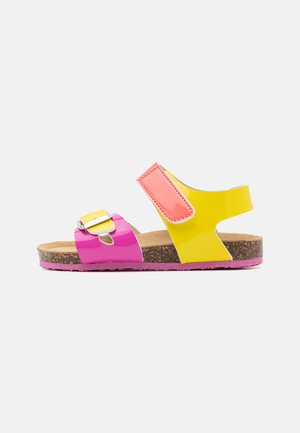 Bunte Sandalen mit glänzenden gelben und pinken Riemen, Korkfußbett, verstellbarem Schnallenverschluss und einer Gummisohle mit pinkem Akzent.