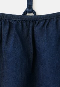 Tissu bleu foncé avec couture froncée près du bord supérieur et une petite sangle bouclée au-dessus, sur un fond clair.