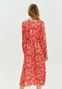 Voľné šaty s dlhým rukávom v odtieňoch ružovej a oranžovej so vzorom listov. Majú opasok v páse a sú stredne dlhé. Ľahká, priesvitná tkanina.